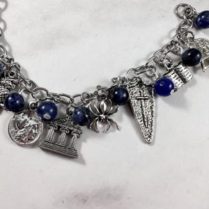 May include: A silver charm bracelet featuring blue beads and a variety of charms, including a spider, a temple, a shield, and a coin.