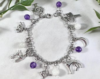 May include: A silver charm bracelet with purple and white beads and charms, including a tree, a crescent moon, a deer, a dog, and an arrow.