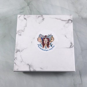 May include: A white marble box with a round sticker featuring a colourful illustration of three women with blue and white clothing. The sticker also includes the text "becatesboutique.etsy.com".