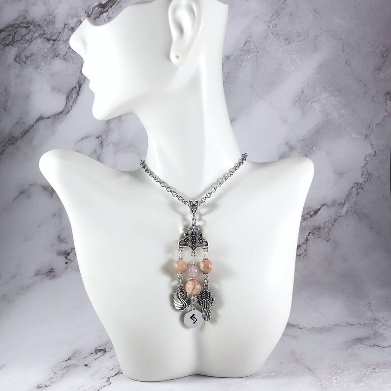 May include: A silver chain necklace with a pendant featuring a silver crown, pink beads, and a silver charm with the number "5" on it.