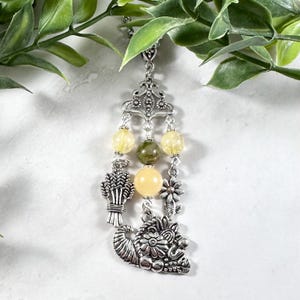 Puede incluir: Un collar de plata con un dije de cornucopia, un dije de gavilla de trigo y cuentas de piedras preciosas amarillas y verdes.
