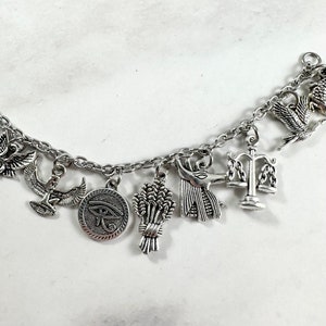 May include: Silver charm bracelet with Egyptian themed charms, including the Eye of Horus, Anubis, a scale of justice, and a sheaf of wheat.