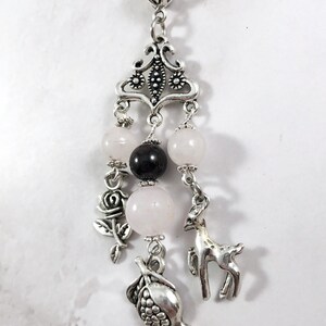 Puede incluir: Un collar de plata con un delicado colgante que presenta una rosa, un ciervo y un granado. El colgante est&aacute; adornado con cuentas rosas y negras.