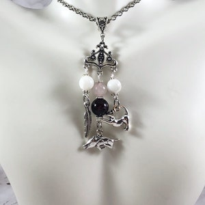 May include: A silver chain necklace with a silver pendant featuring a white, pink, and black bead charm with a silver animal charm hanging from it.