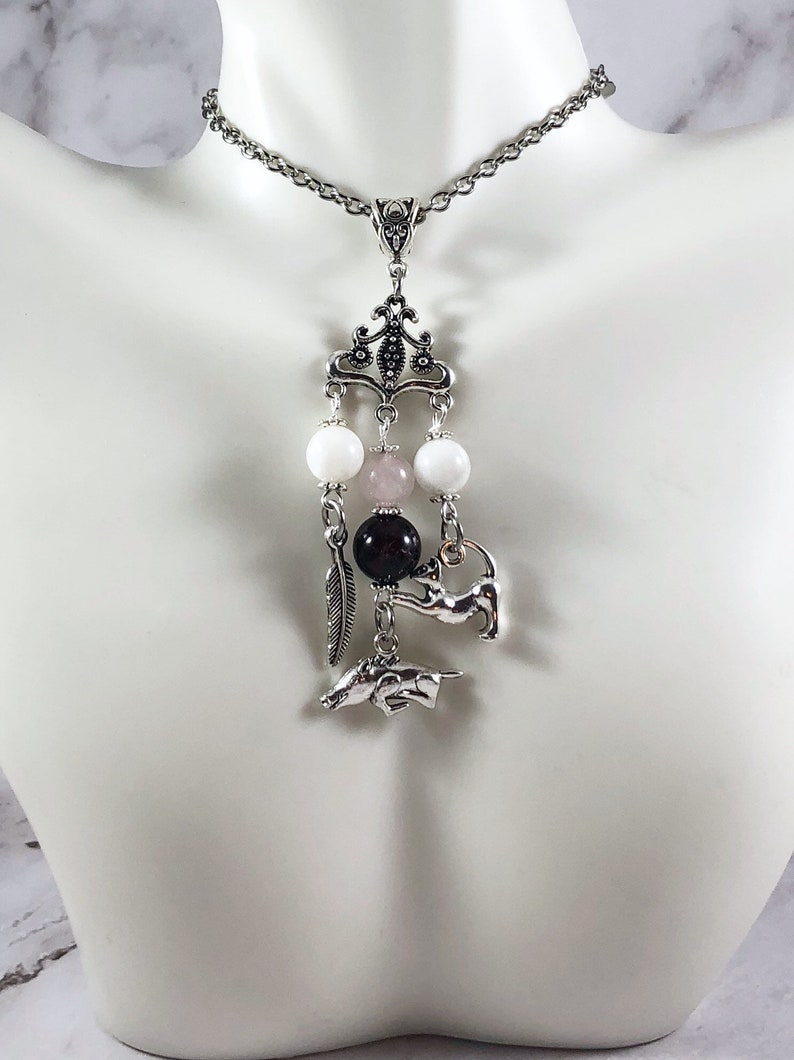 May include: A silver chain necklace with a silver pendant featuring a white, pink, and black bead charm with a silver animal charm hanging from it.
