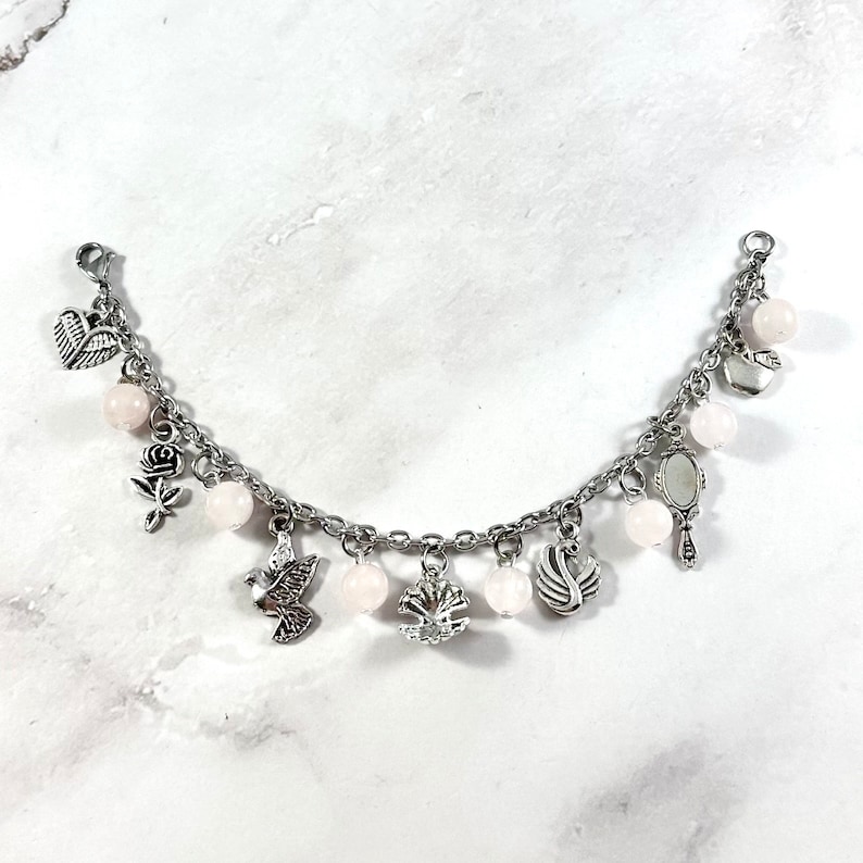 May include: A silver charm bracelet with pink beads and various charms, including a bird, a rose, a heart, a swan, and a mirror.