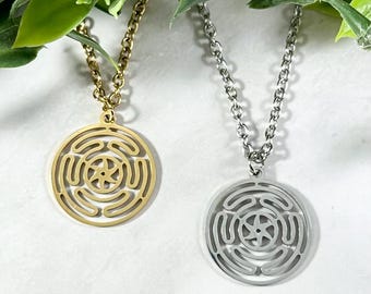 Puede incluir: Dos collares con colgantes circulares que presentan un diseño geométrico. Un collar tiene un colgante dorado y el otro tiene un colgante plateado.