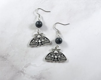 May include: Silver earrings featuring a black stone and a silver moth charm with moon and star details.