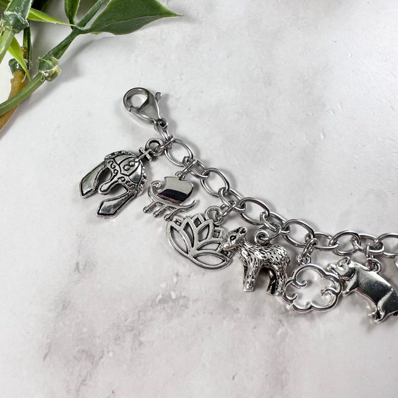 May include: A silver charm bracelet featuring a selection of charms, including a helmet, a lotus flower, a small animal, and a cloud.