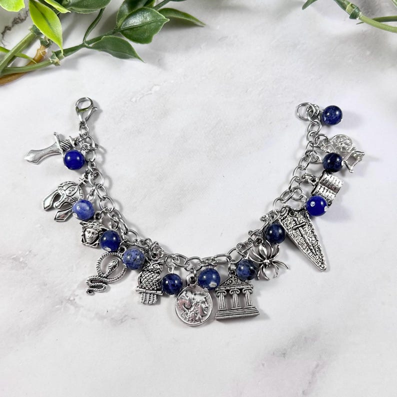 May include: A silver charm bracelet featuring blue beads and a variety of charms, such as a snake, a building, a coin, and a cross.