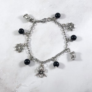 May include: A silver charm bracelet with black beads and charms of spiders, spiderwebs, and spools of thread.