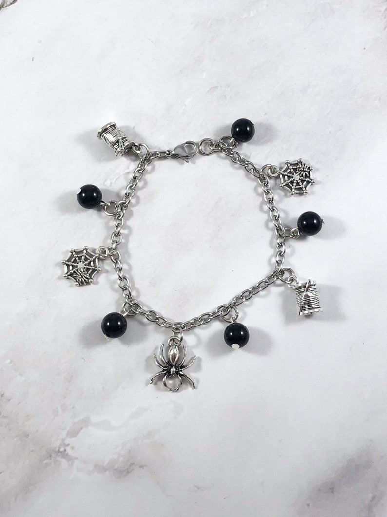 May include: A silver charm bracelet with black beads and charms of spiders, spiderwebs, and spools of thread.