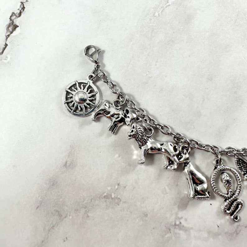 May include: Silver charm bracelet with a sun, lion, snake, and other animal charms.