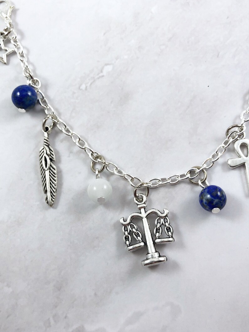 May include: A silver charm bracelet with various charms, including a feather, a scale of justice, a white bead, and blue lapis lazuli beads.