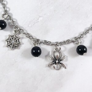 May include: A silver chain bracelet with black beads, a spider charm, and a spiderweb charm.