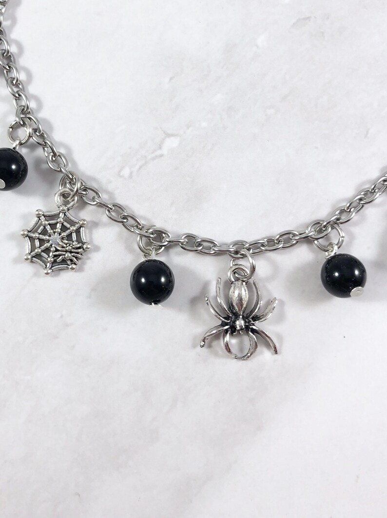 May include: A silver chain bracelet with black beads, a spider charm, and a spiderweb charm.