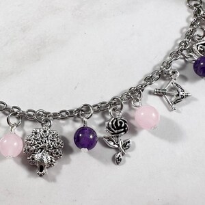May include: A silver charm bracelet with pink and purple beads, a silver tree charm, a silver rose charm, and a silver bow and arrow charm.