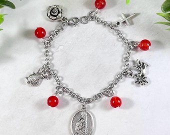 May include: A silver charm bracelet with red beads and charms, including a rose, a cross, a dove, a pitcher, and a religious medal.