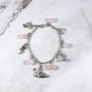 May include: A silver charm bracelet with pink beads and charms, including a swan, a rose, a heart, a leaf, and a bird.