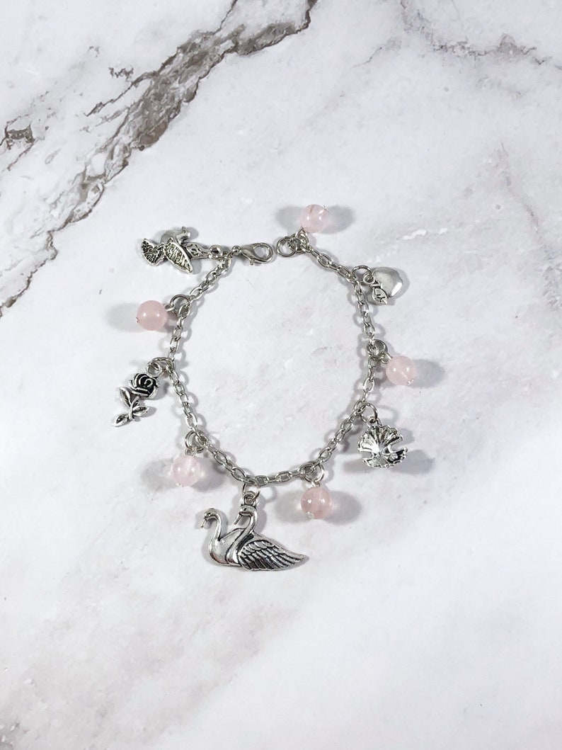 May include: A silver charm bracelet with pink beads and charms, including a swan, a rose, a heart, a leaf, and a bird.