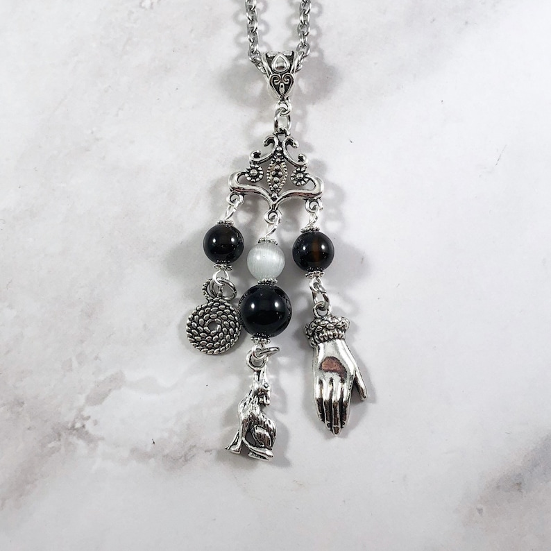 May include: A silver necklace with a chandelier-style pendant featuring black and white beads, a silver hand charm, and a silver animal charm.