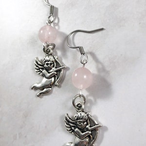 May include: A pair of silver earrings with a pink rose quartz bead and a silver cherub charm on each earring.