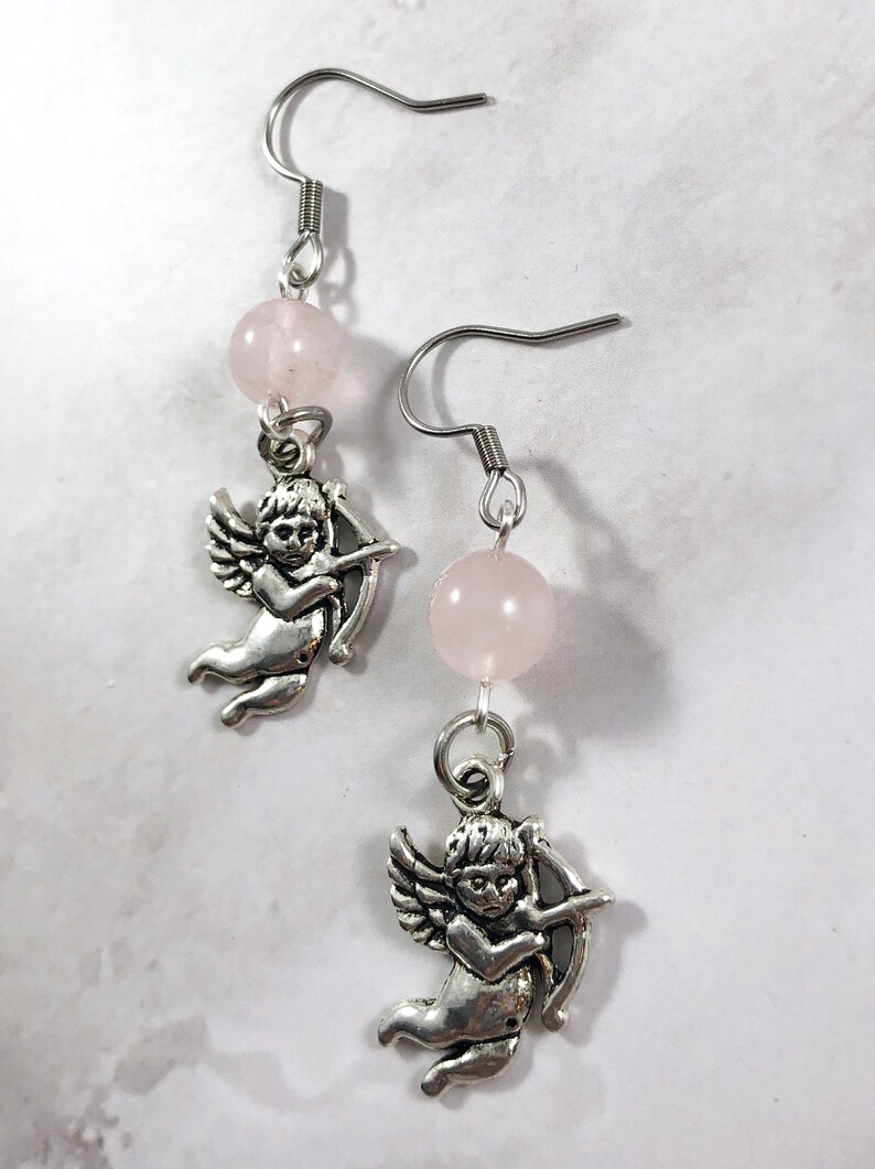 May include: A pair of silver earrings with a pink rose quartz bead and a silver cherub charm on each earring.