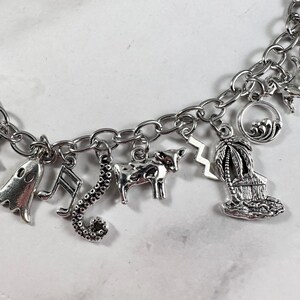 May include: A silver charm bracelet featuring a variety of charms, including a ghost, a musical note, a seahorse, a cow, a lightning bolt, a palm tree, and a hut.