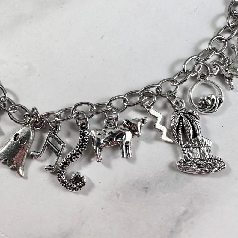 May include: A silver charm bracelet featuring a variety of charms, including a ghost, a musical note, a seahorse, a cow, a lightning bolt, a palm tree, and a hut.