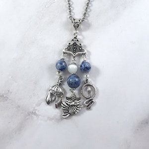 May include: A silver necklace with a pendant featuring a silver owl, snake, and helmet charm. The pendant is adorned with blue and white beads.
