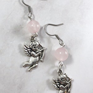 May include: A pair of silver earrings with pink rose quartz beads and a silver cherub charm on each earring.