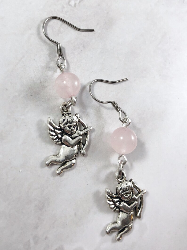 May include: A pair of silver earrings with pink rose quartz beads and a silver cherub charm on each earring.