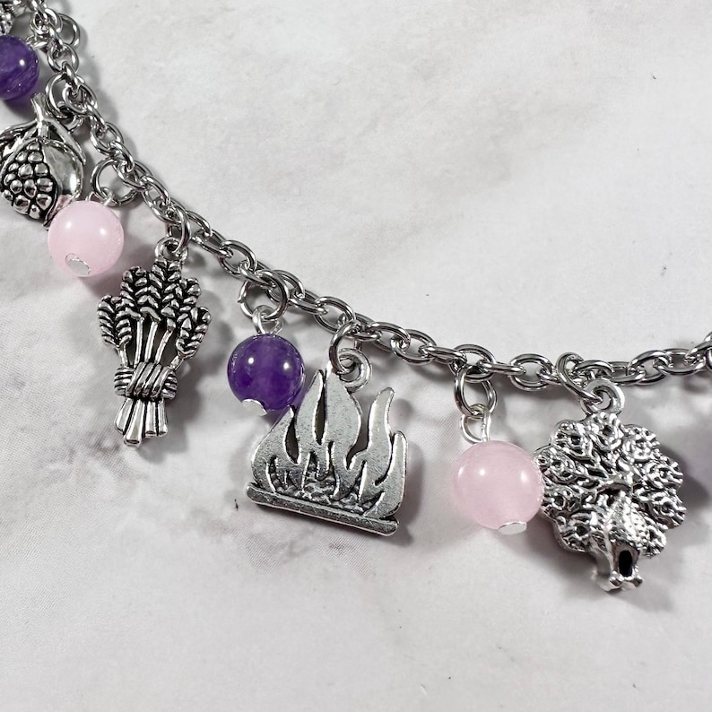 May include: A silver charm bracelet with pink and purple beads, and charms of a wheat sheaf, a flame, and a tree.
