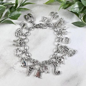 May include: A silver charm bracelet featuring a range of charms, including a ghost, a musical note, a seahorse, a cow, a palm tree, a crescent moon, a pig, a lotus flower, a crown, an axe, a bow and arrow, a house, and a snake.