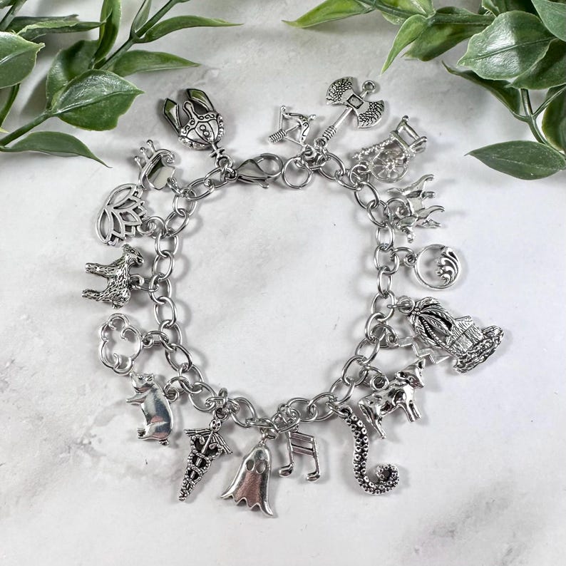 May include: A silver charm bracelet featuring a range of charms, including a ghost, a musical note, a seahorse, a cow, a palm tree, a crescent moon, a pig, a lotus flower, a crown, an axe, a bow and arrow, a house, and a snake.