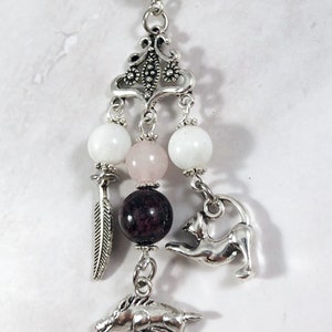 May include: Silver charm necklace with a pink, white, and dark red bead. The charm features a cat, a horse, and a feather.