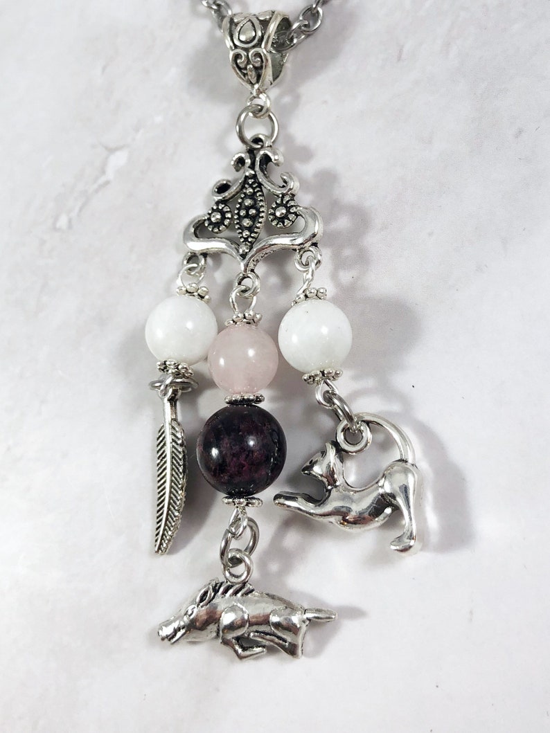 May include: Silver charm necklace with a pink, white, and dark red bead. The charm features a cat, a horse, and a feather.