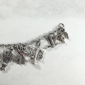 May include: A silver charm bracelet with various charms, including a scale of justice, a wheat sheaf, an ankh, and a bird.