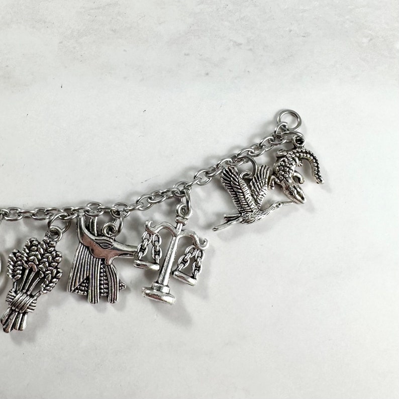 May include: A silver charm bracelet with various charms, including a scale of justice, a wheat sheaf, an ankh, and a bird.