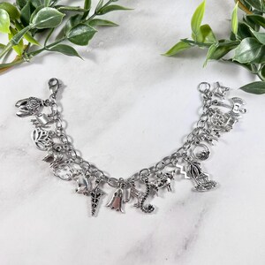 May include: A silver charm bracelet featuring a range of charms, including a ghost, a seahorse, a palm tree, a cow, and a unicorn. The bracelet is displayed against a white backdrop.