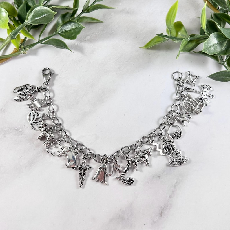 May include: A silver charm bracelet featuring a range of charms, including a ghost, a seahorse, a palm tree, a cow, and a unicorn. The bracelet is displayed against a white backdrop.