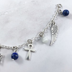 May include: A silver charm bracelet with multiple charms, including a wing, an ankh, and blue beads.