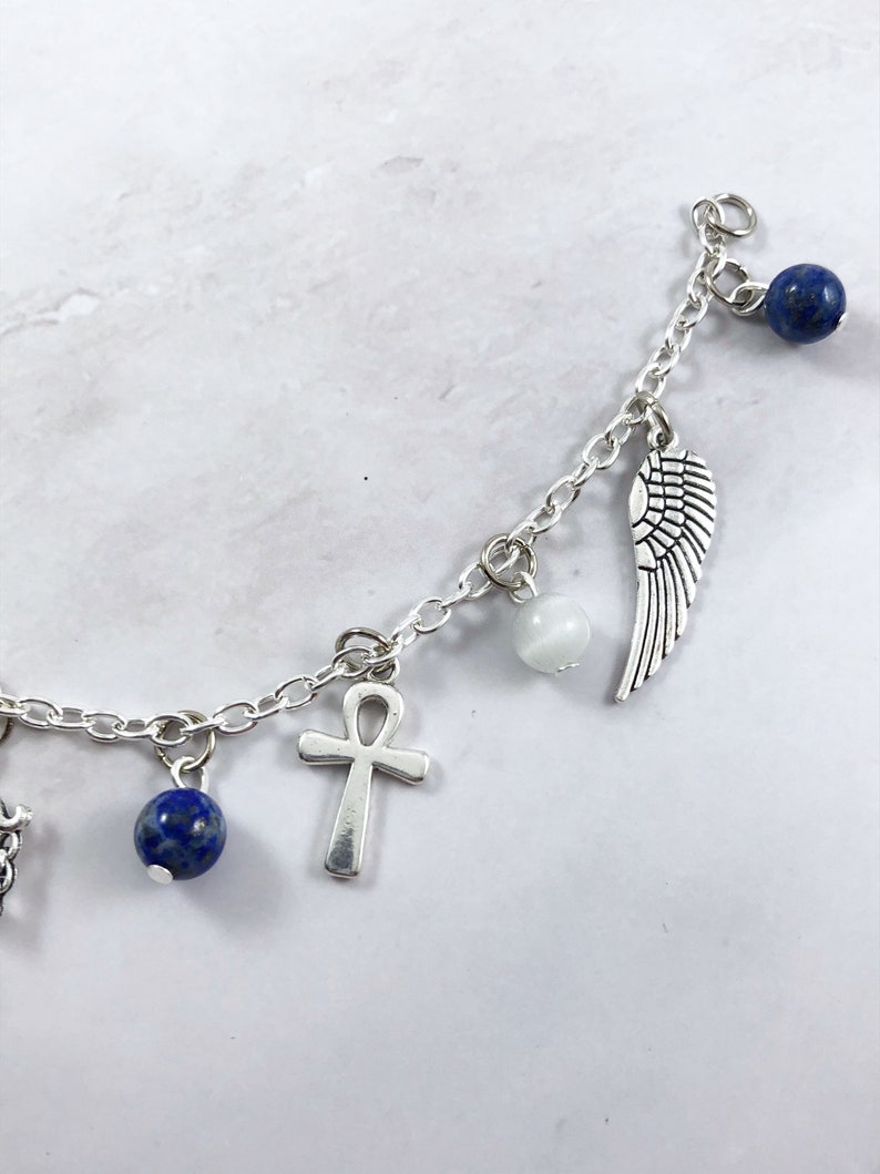 May include: A silver charm bracelet with multiple charms, including a wing, an ankh, and blue beads.