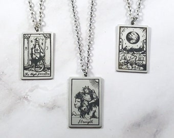 May include: Three silver necklaces with rectangular pendants featuring black and white illustrations of tarot cards. The cards are "The High Priestess", "Strength", and "The Moon".