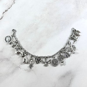 May include: Silver charm bracelet with various Egyptian symbols, including an ankh, a scarab beetle, a cobra, a sun disc, a winged sun, a lion, a goddess, a scale, a wheat sheaf, and the Eye of Horus.