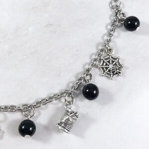 May include: A silver charm bracelet with black beads and silver charms, including a spider web, a spool of thread, and a small bead.
