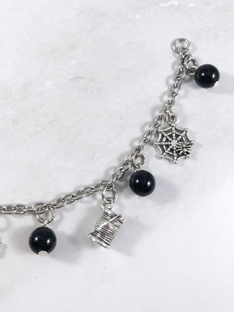 May include: A silver charm bracelet with black beads and silver charms, including a spider web, a spool of thread, and a small bead.