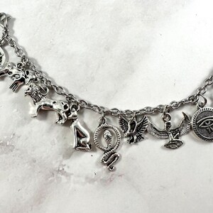 May include: Silver charm bracelet with multiple Egyptian-themed charms, including a lion, a snake, an ankh, a scarab beetle, and an eye of Horus.