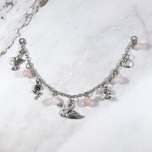 May include: A silver charm bracelet with pink beads and various charms, including a swan, a rose, a heart, a dove, and a tree.