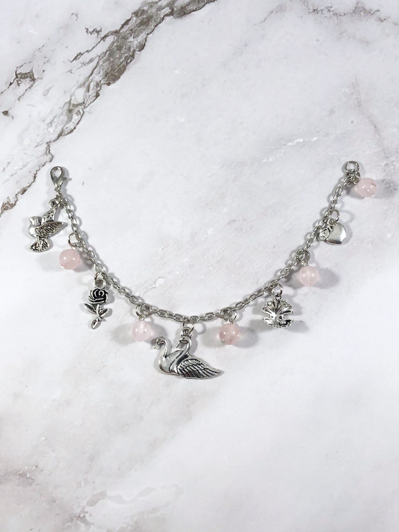 May include: A silver charm bracelet with pink beads and various charms, including a swan, a rose, a heart, a dove, and a tree.